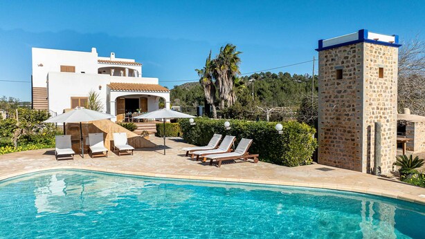 Ein Poolbereich mit Liegestühlen und Sonnenschirmen, ein Steinhaus und ein weißes Haus mit Ziegeldach.