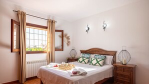 Ein ordentlich bezogenes Bett mit weißer Bettdecke, zwei Nachttische mit Lampen, ein Fenster mit Vorhängen und eine Heizung.