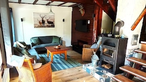 Una sala de estar acogedora con un sofá, sillones de mimbre, una mesa de madera, una chimenea y una cabeza de ciervo decorativa.