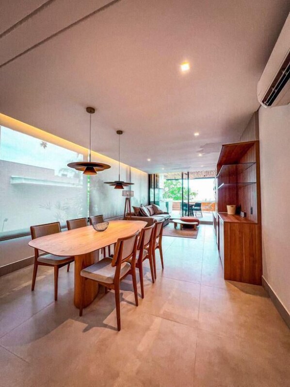 A modern dining area with a wooden table and chairs, pendant lighting, and a view of the outdoors.