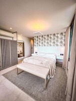 Um quarto moderno com uma cama grande, um banco, um guarda-roupa e um espelho.