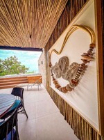 Um interior moderno com teto de bambu, uma obra de arte abstrata na parede e uma área de refeições com cadeiras e mesa.