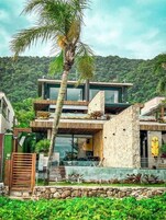 Uma casa moderna de dois andares com fachada de pedra, janelas grandes e um jardim tropical.