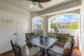 A laundry room with a table and chairs, a ceiling fan, and a view of houses through arched windows.