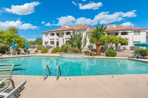 A swimming pool with a 5-foot depth marker, lounge chairs, and a building with a tiled roof in the background.