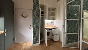 A compact room with a wooden floor, a washing machine, and a small desk with a chair. - Comfort chic - Duomo in 5 minutes (Milano)
