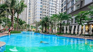 A swimming pool surrounded by palm trees and modern buildings. - Cozy- Vinhomes Central Park Apartments (Ho Chi Minh City)