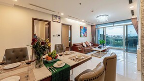 A modern dining area with a table set for two, a vase of flowers, and a city view through large windows. - Cozy- Vinhomes Central Park Apartments (Ho Chi Minh City)