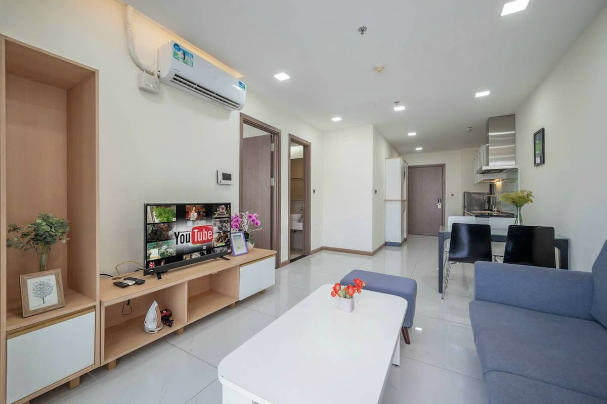 Una sala moderna con un televisor de pantalla plana, una mesa de centro y un sofá. Hay una cocina con un refrigerador y una mesa de comedor.