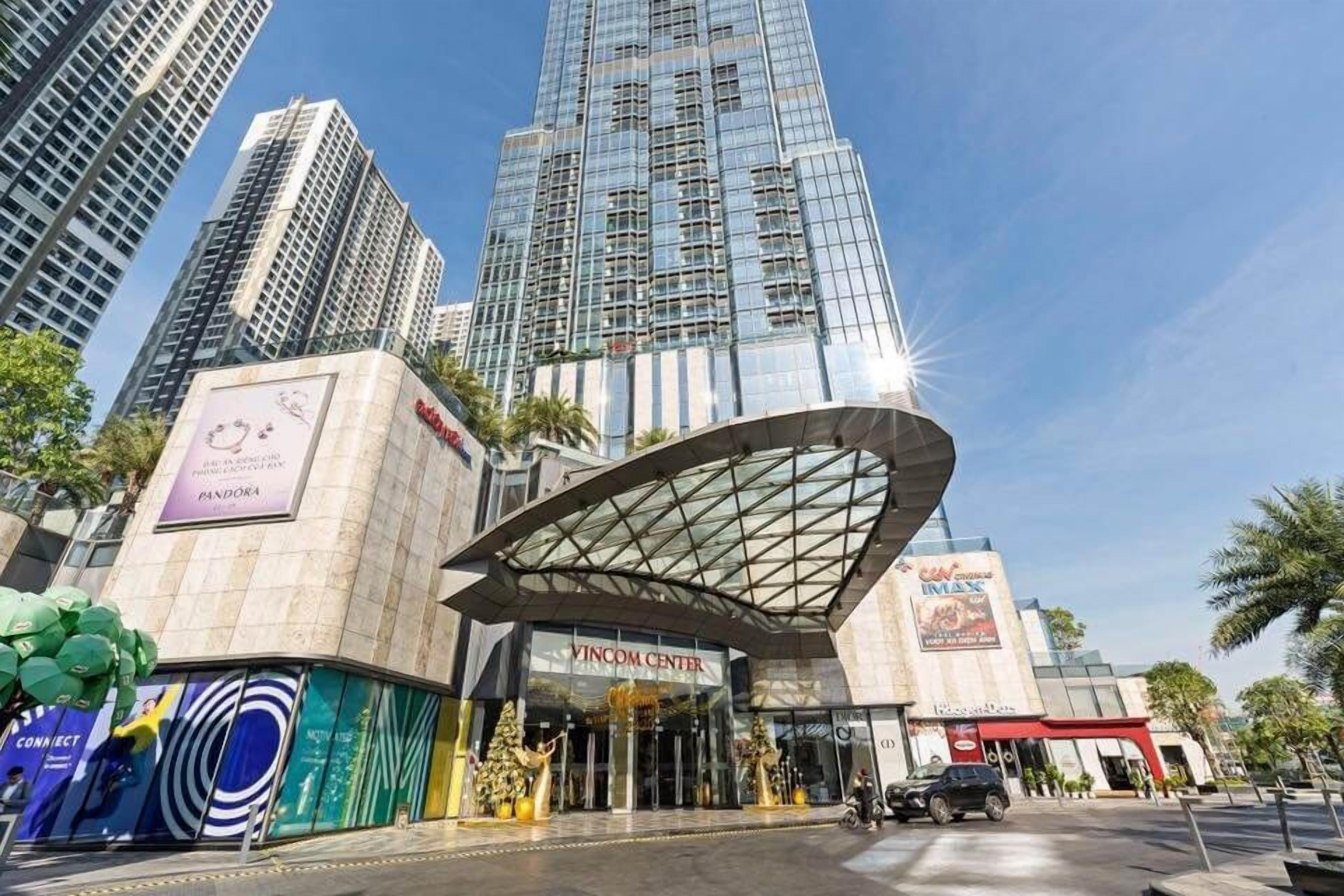 A modern building with a curved glass entrance, a sign for 'Vincom Center', and a 'Pandora' sign on the left.