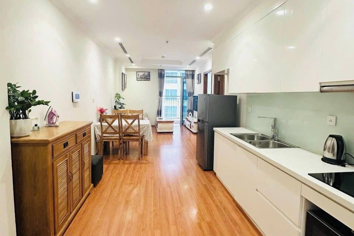 Una cocina moderna con suelo de madera, armarios blancos y un comedor con mesa y sillas.