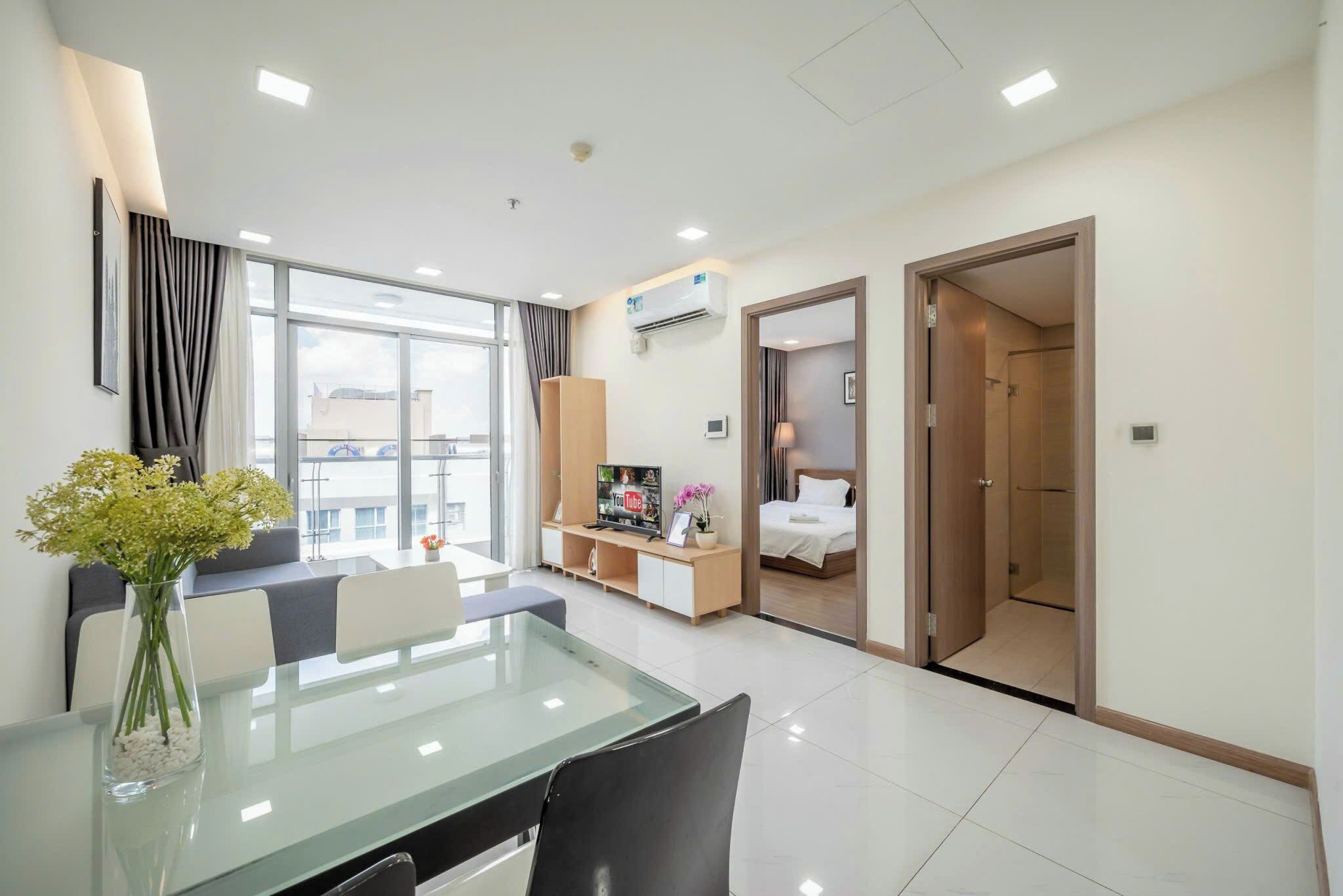 Una habitación de hotel moderna con una mesa de comedor de cristal, un sofá, un televisor y una cama.