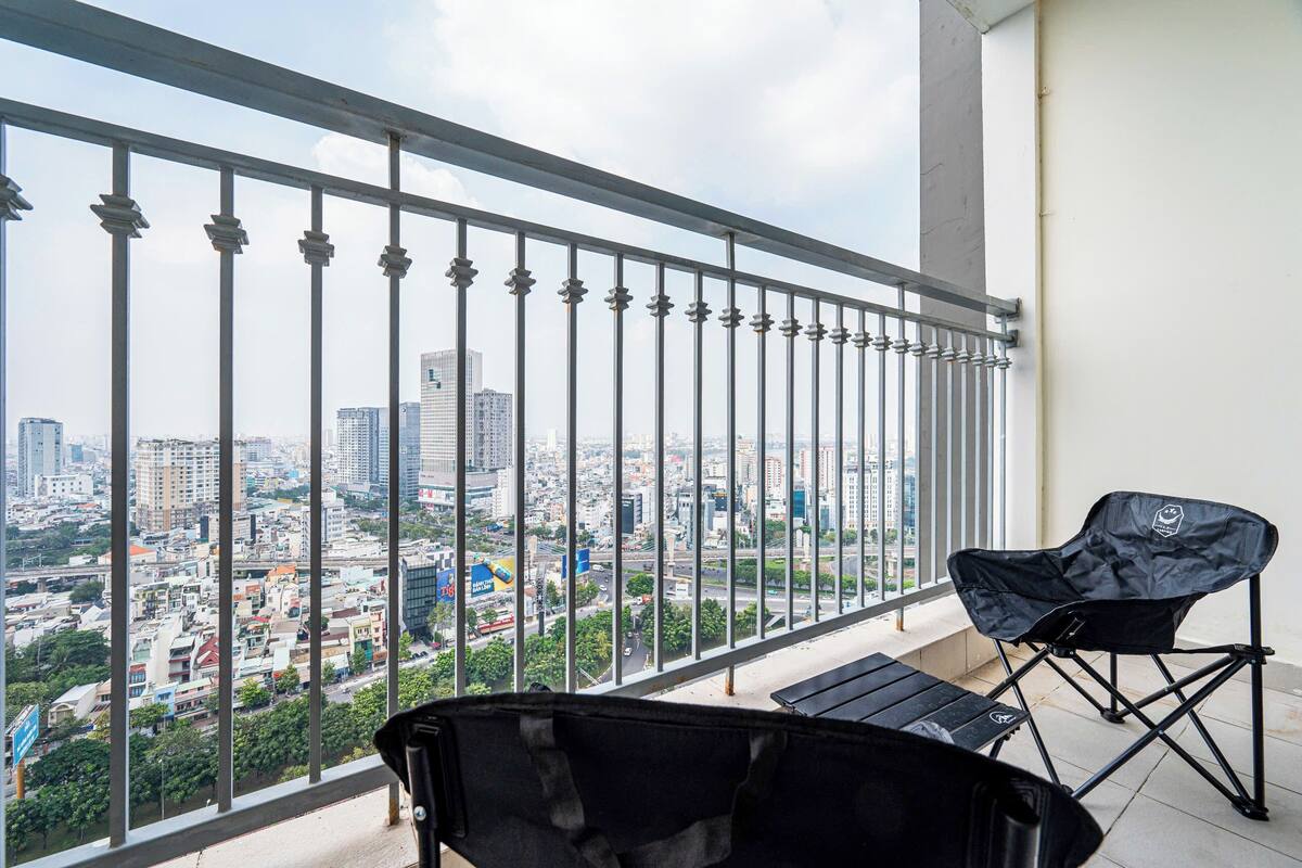 Un balcón con vista a la ciudad, una silla plegable negra y una bolsa negra.