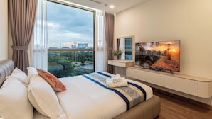 A modern hotel room with a large bed, a TV on a mounted shelf, and a city view through large windows. - Cozy- Vinhomes Central Park Apartments (Ho Chi Minh City)