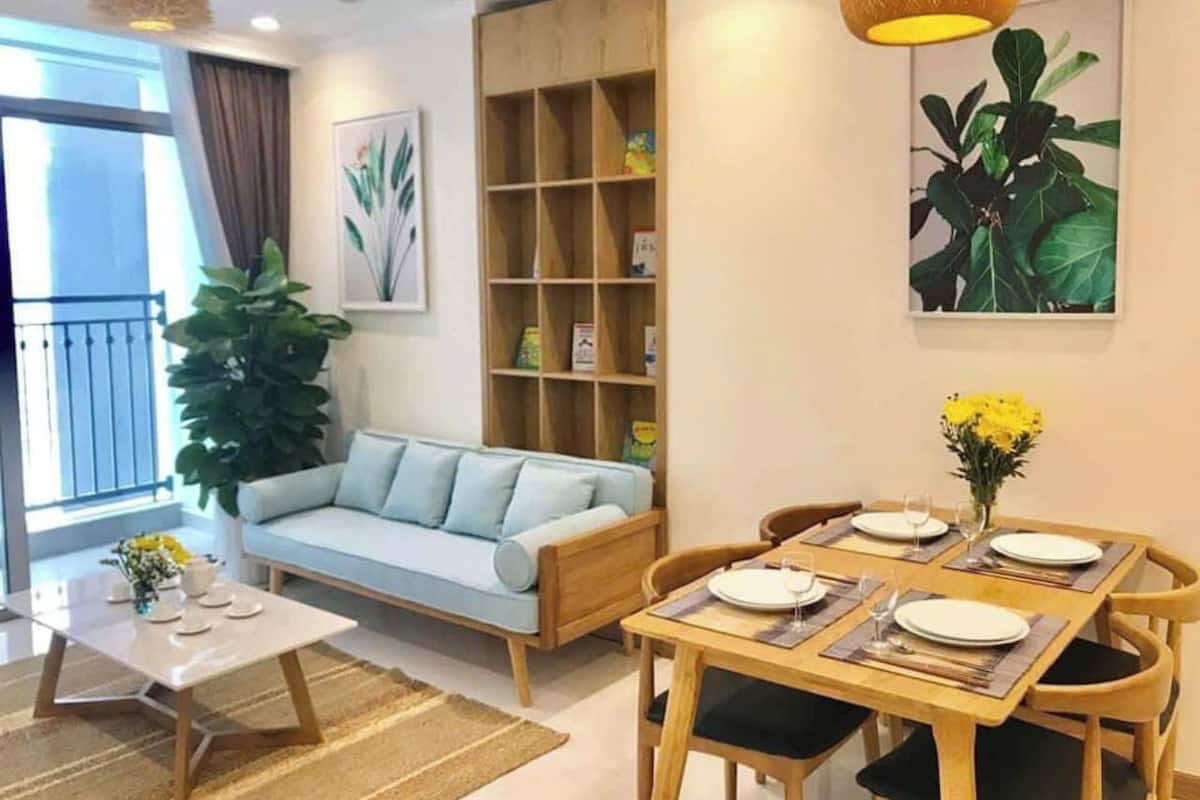 Una sala de estar con un sofá, una mesa de comedor para cuatro personas, una estantería y una planta grande.