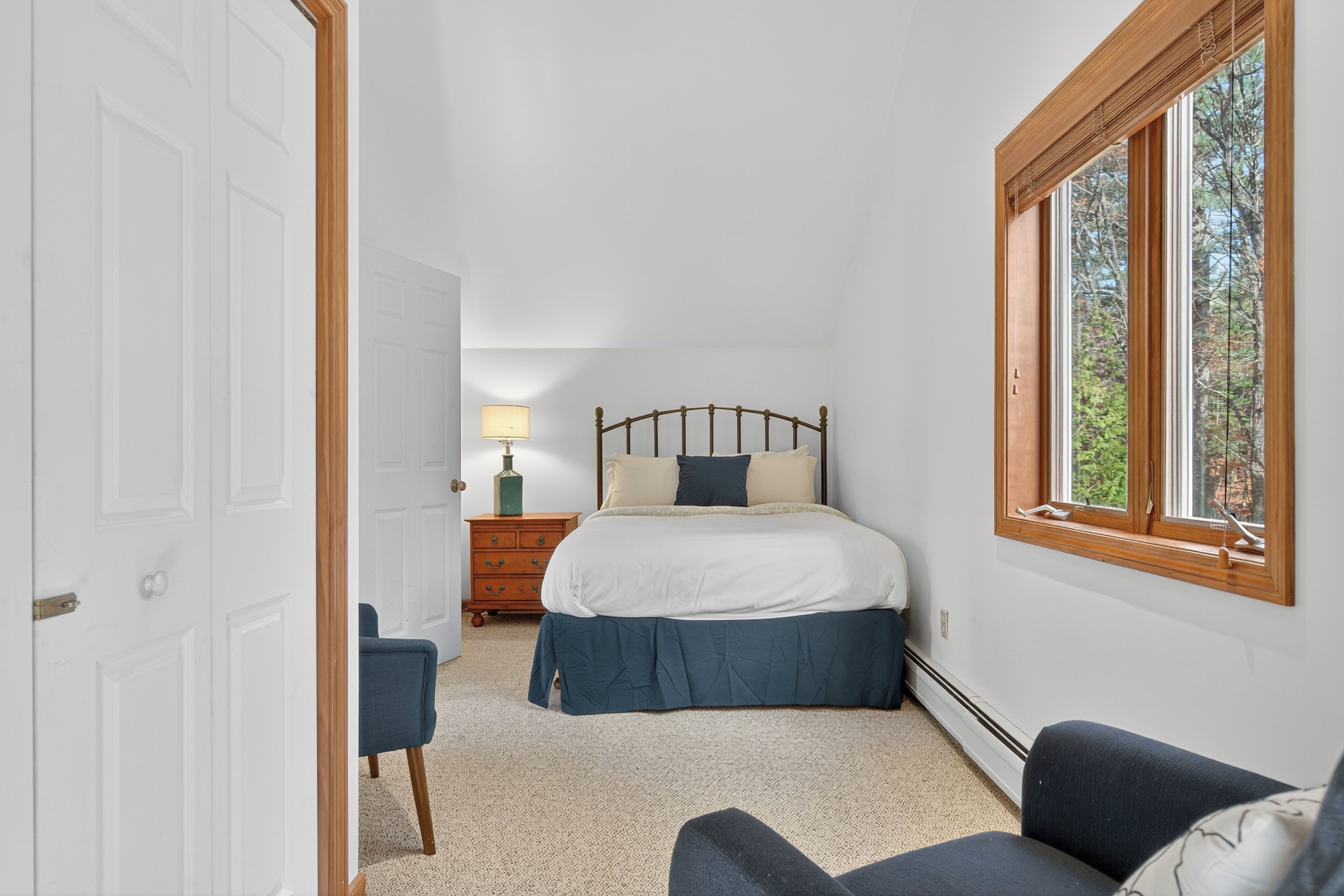 Ein Schlafzimmer mit Bett, Nachttisch, Lampe, Stuhl und Fenster.