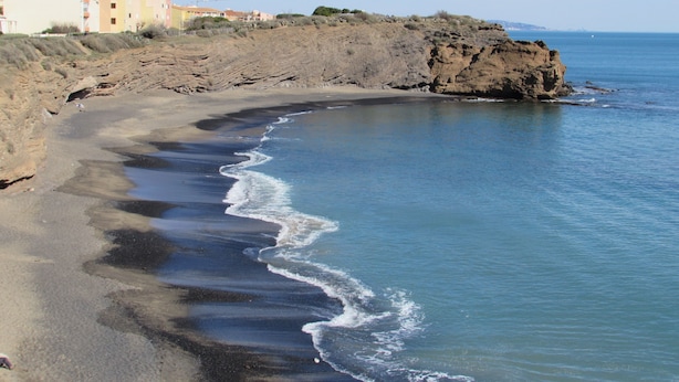 A coastal landscape with a rocky shoreline, a sandy beach, and buildings in the background. - 40m² apartment ideal for 2 or 4.  50 m from the sea. quiet area. (Agde)