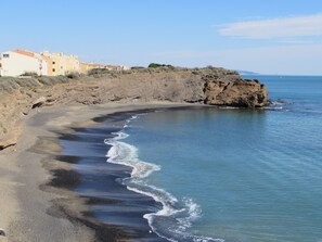 A coastal landscape with a rocky shoreline, a sandy beach, and buildings in the background. - 40 m² apartment, ideal for 2 or 4 people. 50 m from the ocean. Quiet location. (Agde)