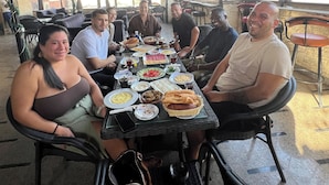 A group of people seated around a table with food and drinks, in a covered outdoor area with hanging plants and star decorations. - Topaz Pyramids view inn  (Giza)