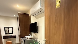 A hotel room with a wooden door, a flat-screen TV, a minibar, a refrigerator, a potted plant, and a small table with a tray. - Topaz Pyramids view inn  (Giza)