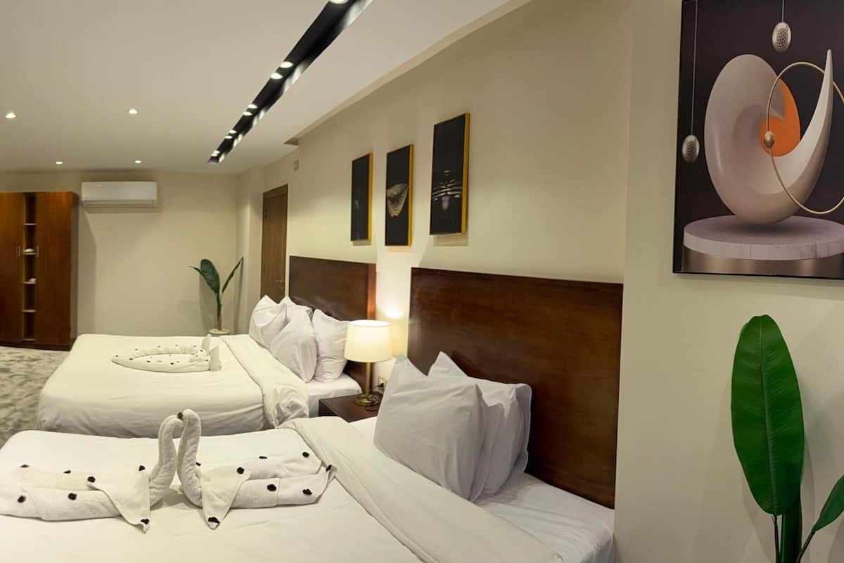 A hotel room with two beds, a flat-screen TV, a minibar, and artwork on the walls.