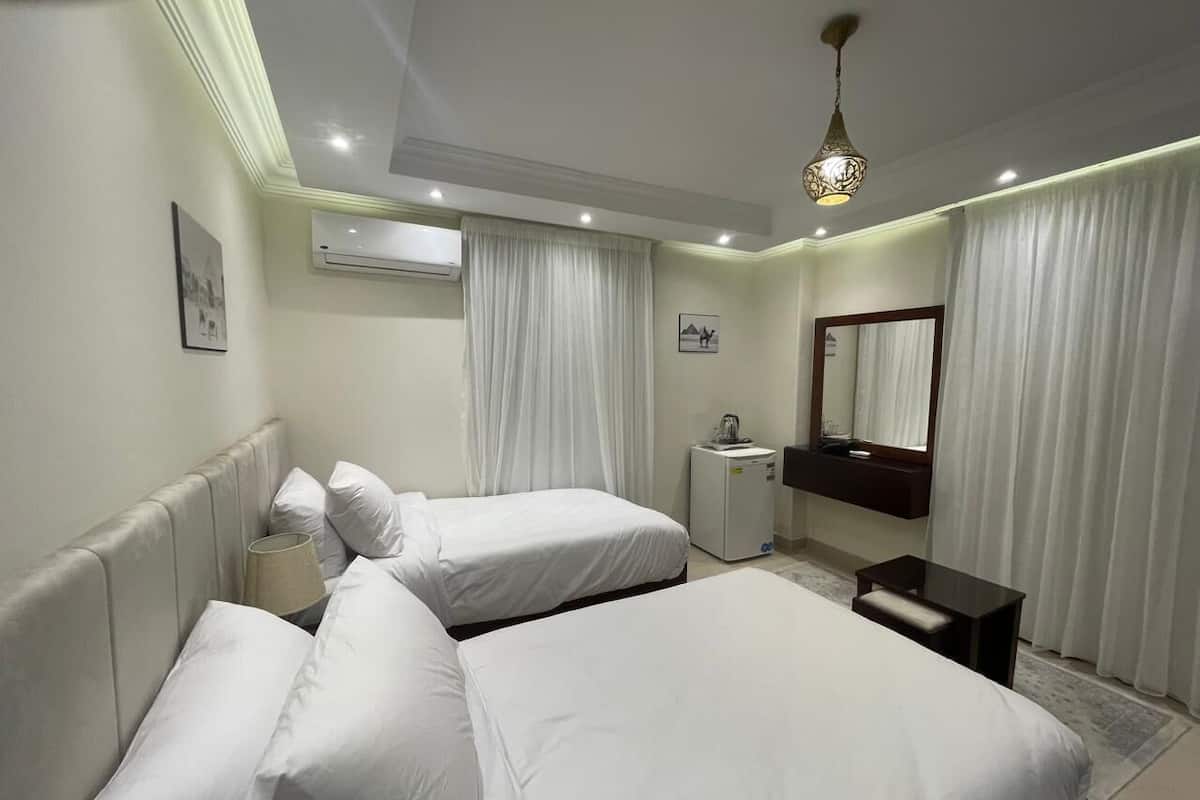 A hotel room with two beds, a small desk, a mirror, and an air conditioning unit.