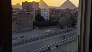 A view of the pyramids at sunset from a window overlooking a street with buildings and a road. - Topaz Pyramids view inn  (Giza)