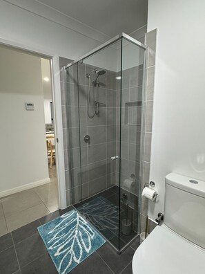 Ein modernes Badezimmer mit einer gläsernen Duschkabine, einer Toilette und einem Waschbecken.