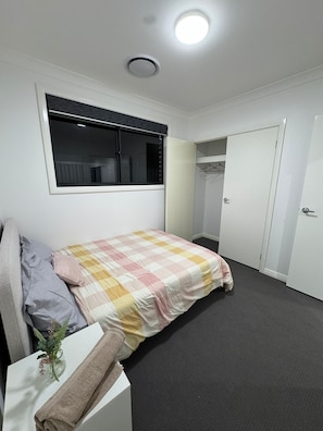 Ein Schlafzimmer mit Bett, Fenster, Schrank und Tür.