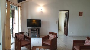 Una sala de estar con televisor, dos sillas de madera, una mesa de centro y una puerta que da a otra habitación.