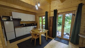 Een houten chalet van binnen met een keuken, een eethoek en schuiframen die uitkomen op een tuin.