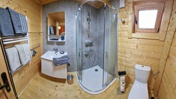 A compact wooden bathroom with a glass-enclosed shower, a sink, and a toilet.