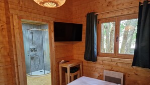 Een houten kamer met een bed, een klein tafeltje, een televisie en een douche.