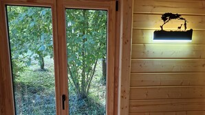 Een houten interieur met een schuifdeur van glas die uitkomt op een buitenruimte, een klein tafeltje met een vaas, en een wandlamp.
