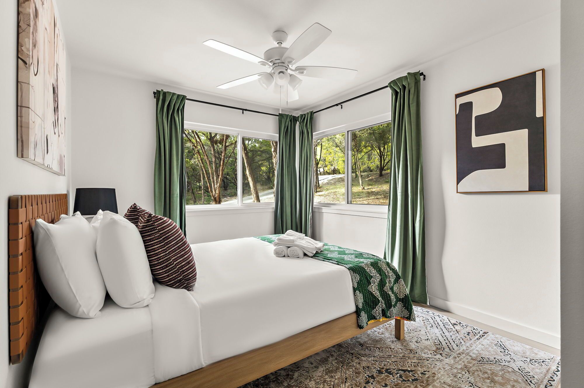 Un dormitorio con cama, ventilador de techo y ventanas amplias con cortinas.