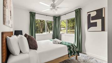Un dormitorio con cama, ventilador de techo y ventanas amplias con cortinas.