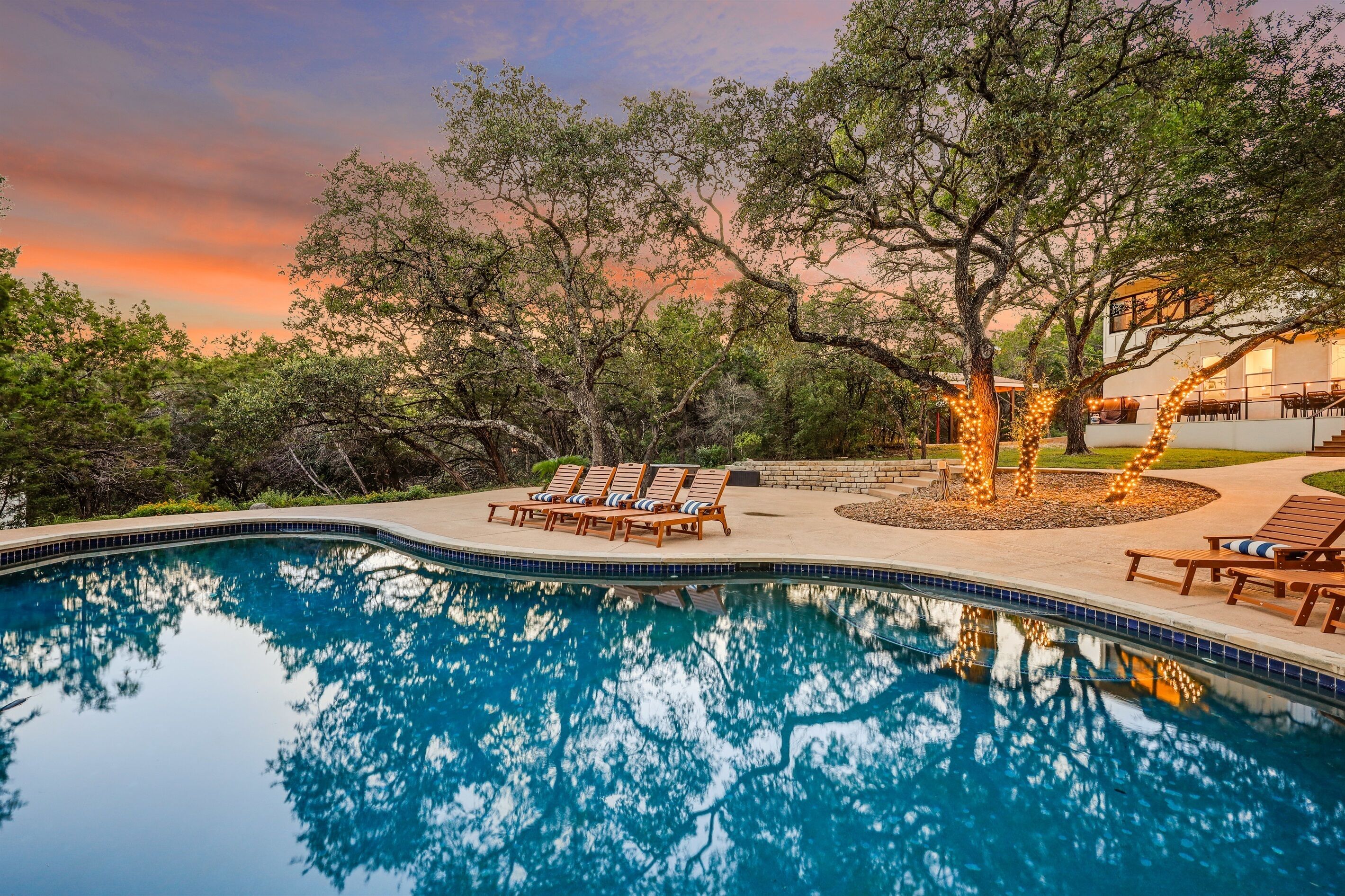 Una piscina con sillones de descanso y un árbol al fondo.