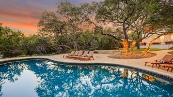 Una piscina con sillones de descanso y un árbol al fondo.