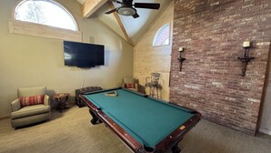 A pool table in a room with a brick wall, a ceiling fan, and a television mounted on the wall. - Spacious 6-bedroom 6.5 bath house in charming Crested Butte with gym and hot tub (Crested Butte)