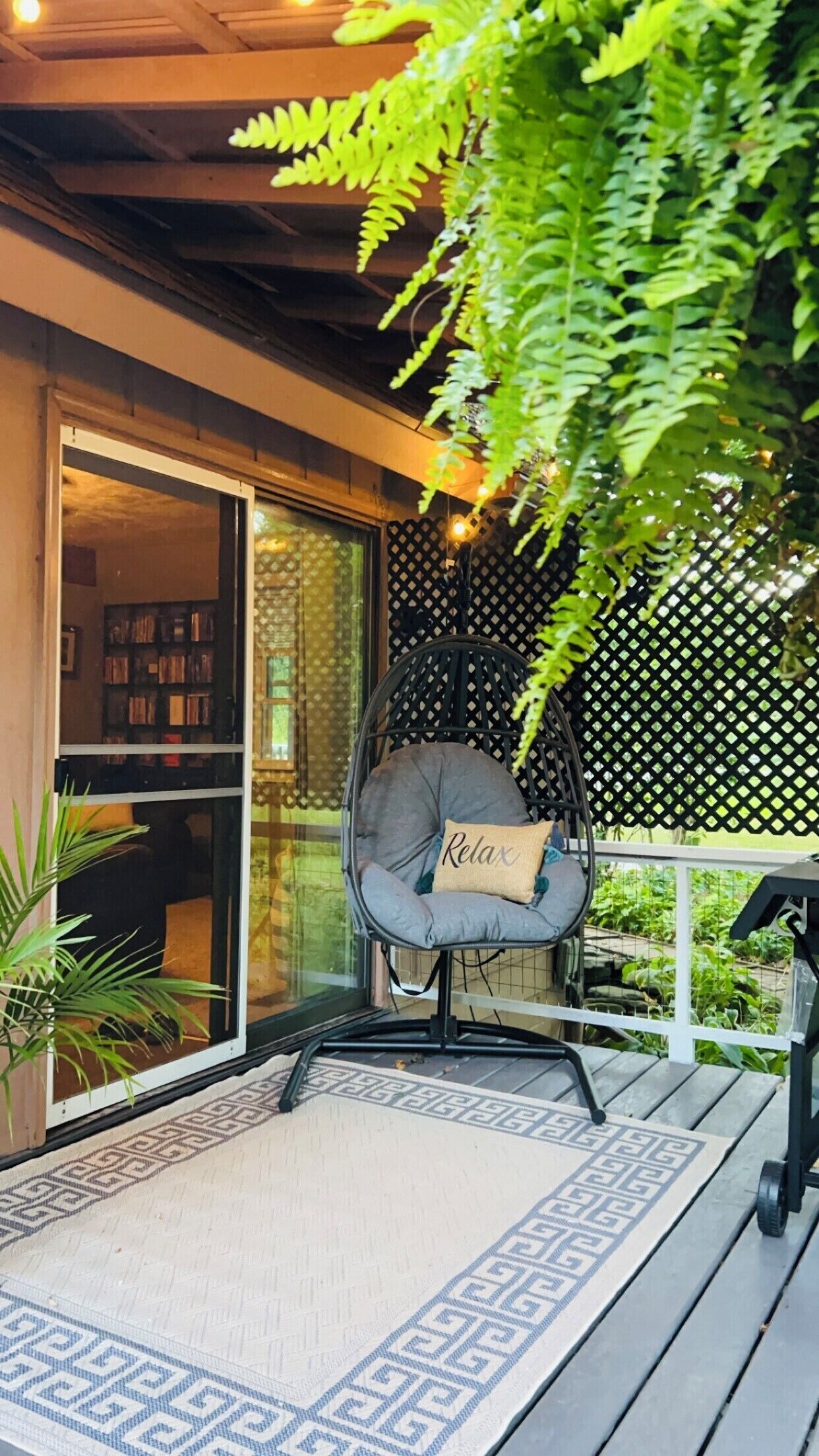 Un rincón exterior acogedor con una silla acolchada, un tapete estampado y una terraza de madera.