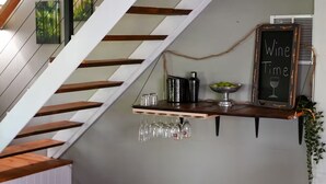 Un escalier avec des marches en bois et une rampe blanche. On y trouve une étagère avec un panneau noir sur lequel est écrit « Wine Time » et un bol rempli de citrons.