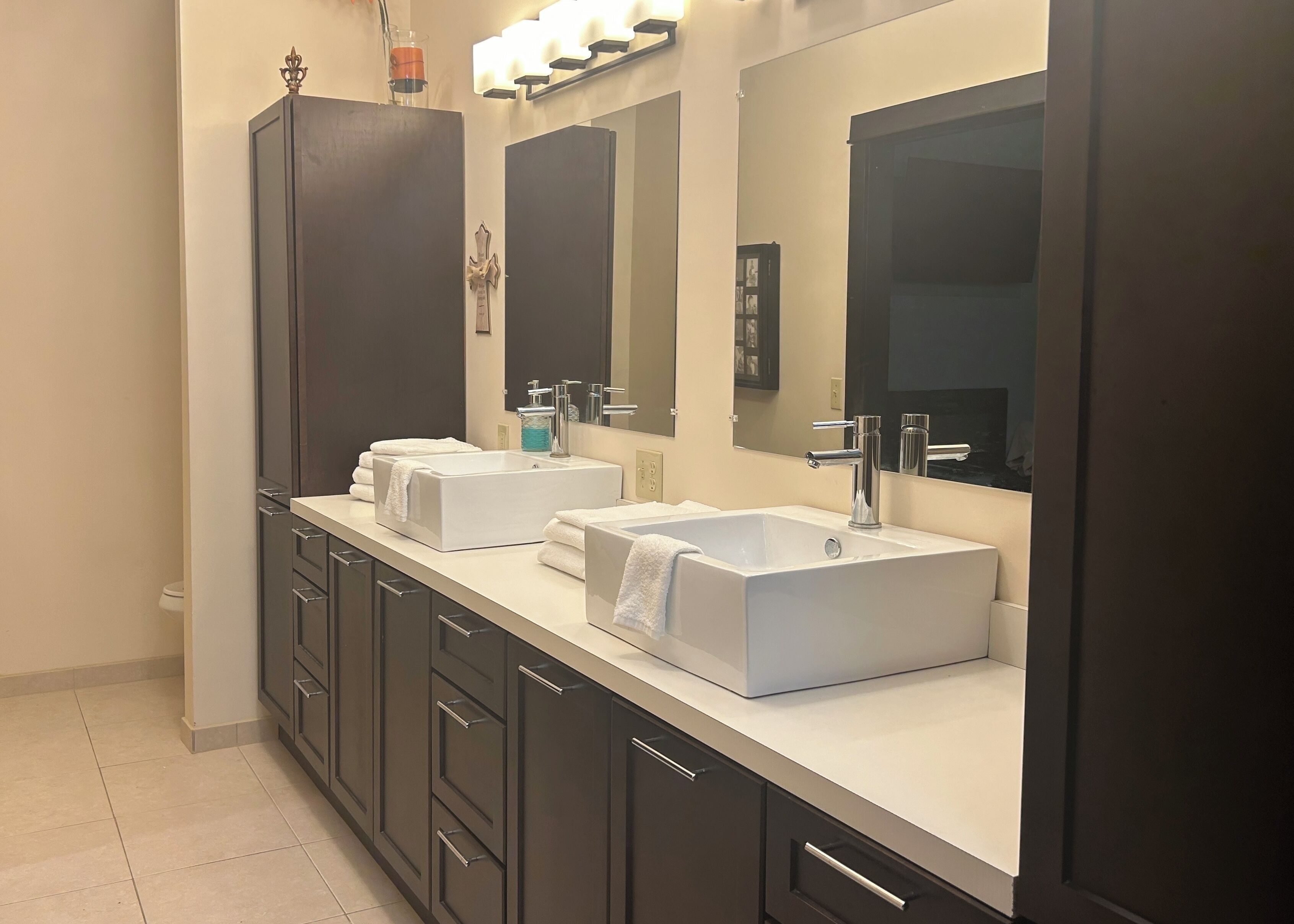 A modern bathroom with two white sinks, dark cabinets, and a large mirror.