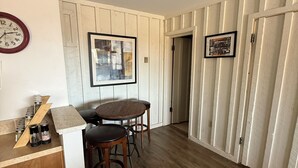 Une cuisine compacte avec un plan de travail en bois, un réfrigérateur blanc, une table à manger avec quatre chaises et une horloge murale.