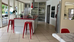 Una cocina moderna con una isla de vidrio, taburetes rojos y vistas al exterior.