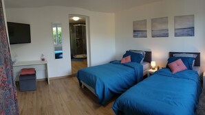 A hotel room with two beds, a desk, a TV, and artwork on the wall.