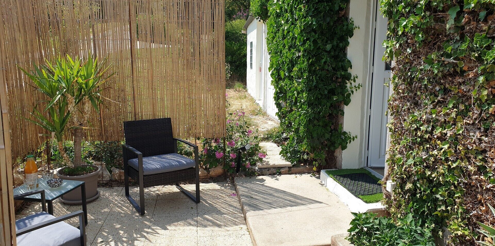 Eine Terrasse mit Korbstuhl, kleinem Tisch, Flasche und Glas sowie Blumentöpfen.
