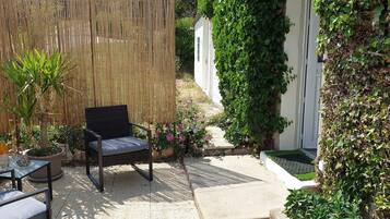 Eine Terrasse mit Korbstuhl, kleinem Tisch, Flasche und Glas sowie Blumentöpfen.
