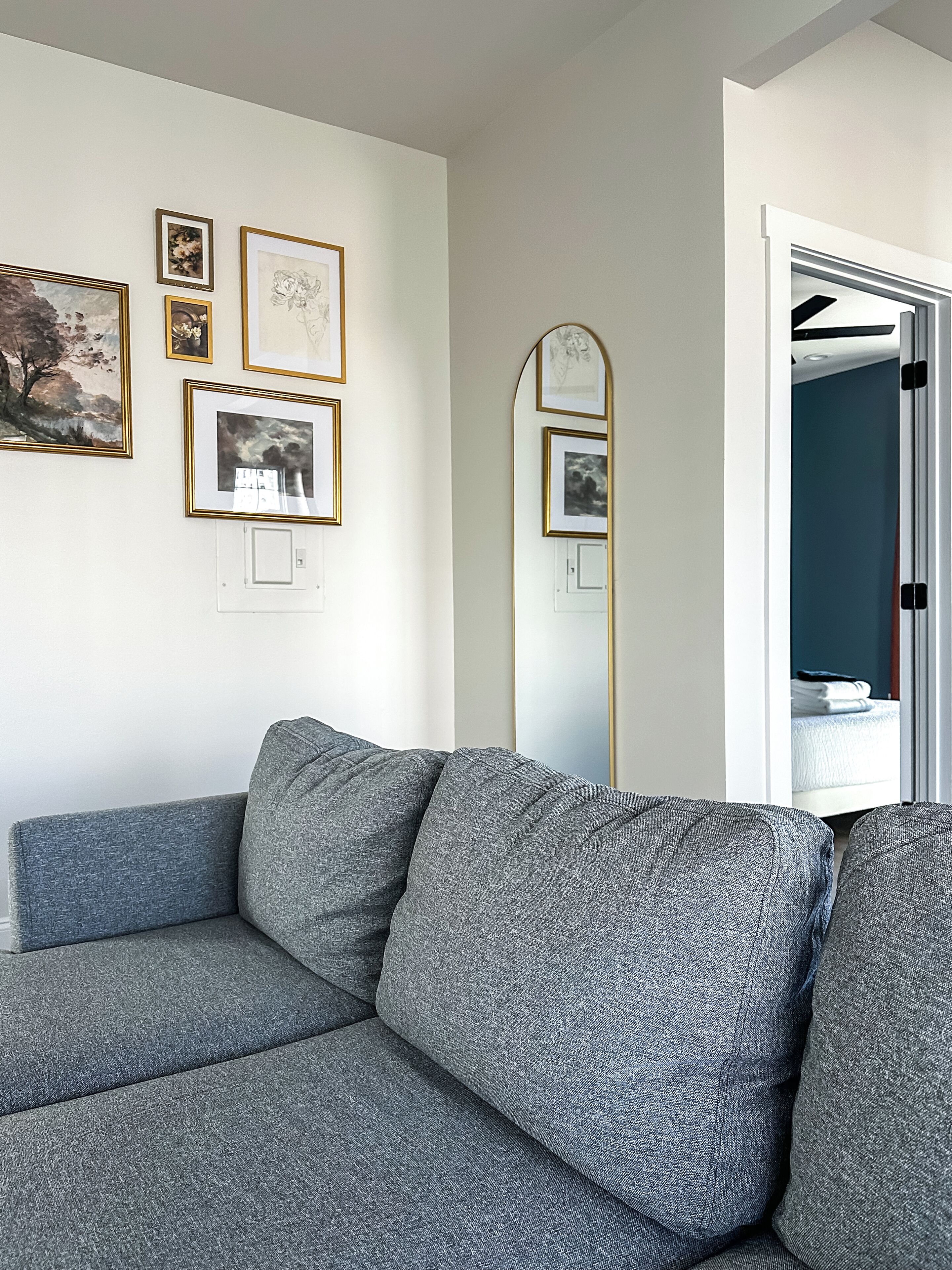 A modern living room with a grey sectional sofa, a large mirror, and framed artwork on the wall.