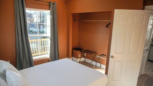 A bedroom with a bed, a window with curtains, a door, and a drying rack. - StayAE - Flamingo House (Baton Rouge)