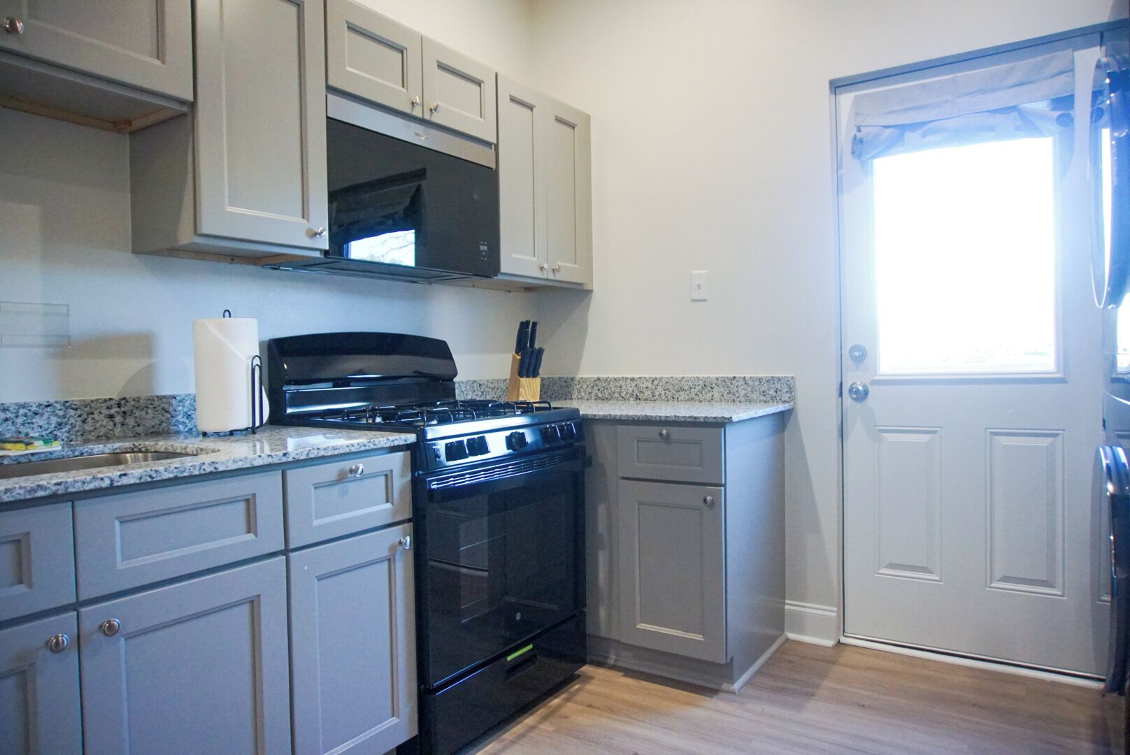 A kitchen with grey cabinets, a black stove, and a microwave.